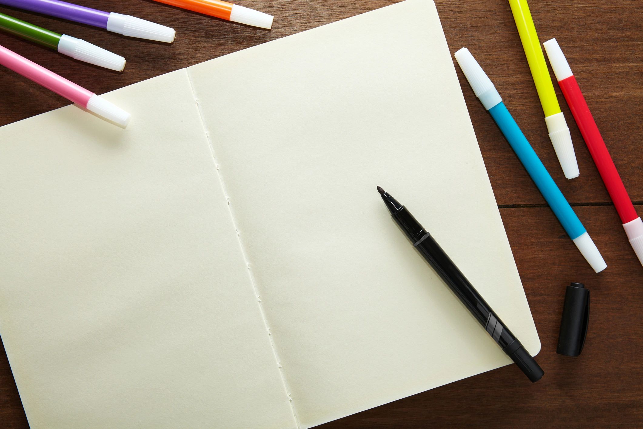 Open sketchbook with markers on a wooden table