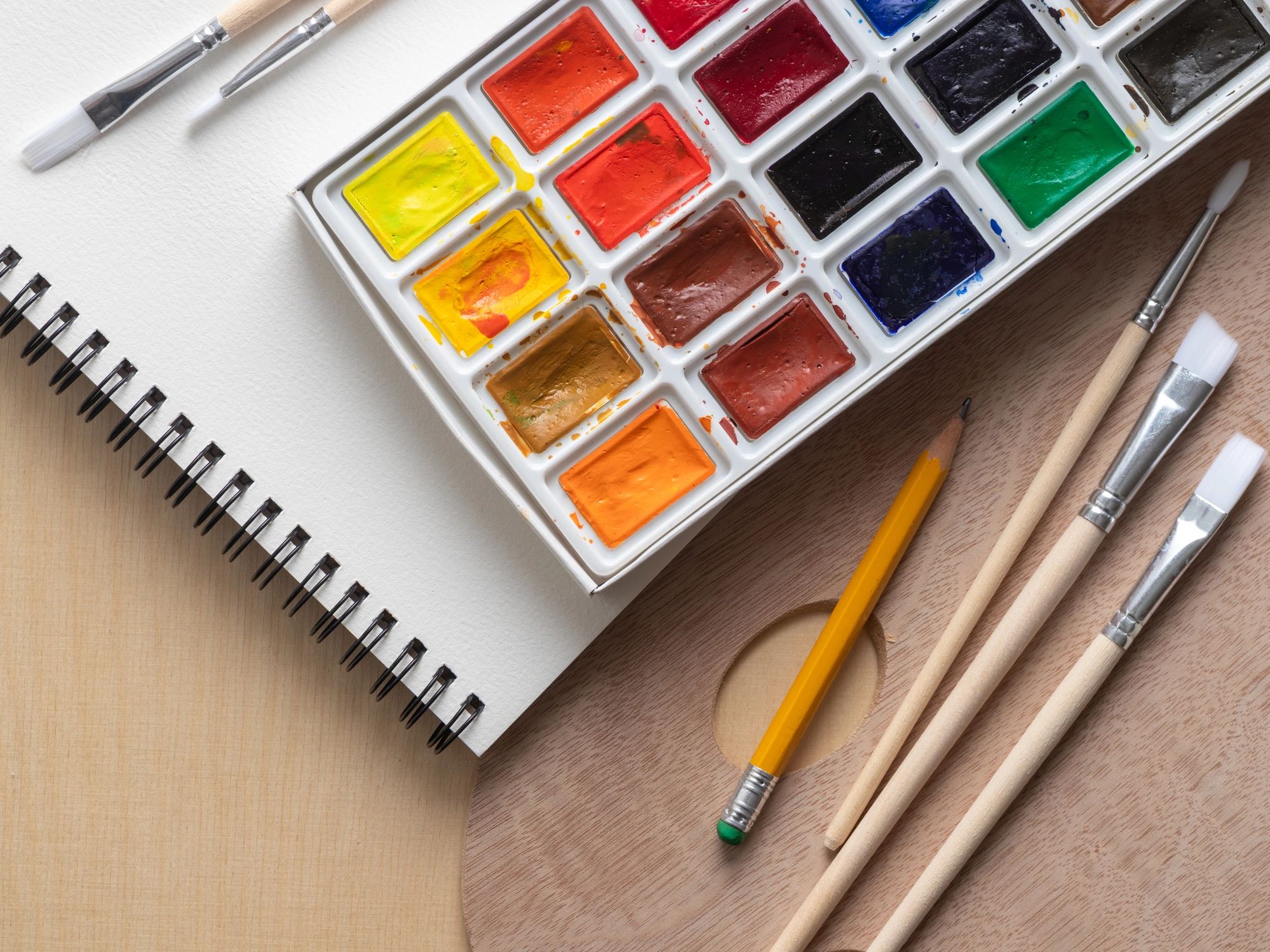 Watercolor supplies beside a spiral-bound sketchbook